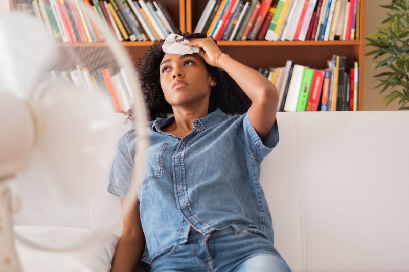 Woman sweating and fanning herself on her couch.
