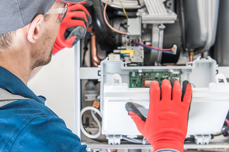 Schedule Your Annual Furnace Inspection Now. Photo of a technician performing maintenance inside a heating furnace.